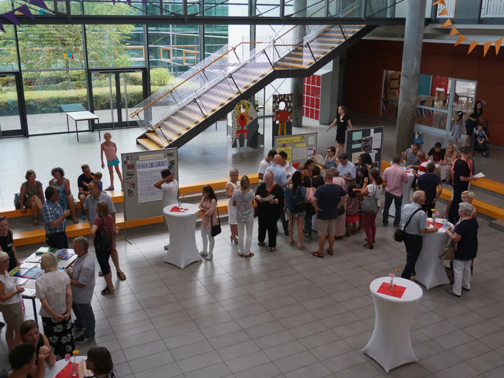 Blick von oben ins Foyer mit Stehtischen und Gästen.